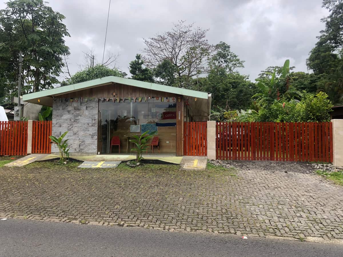 La recepción de Le Petit Hôtel sobre la ruta 702, con cerca de madera naranja — así se ve desde la calle